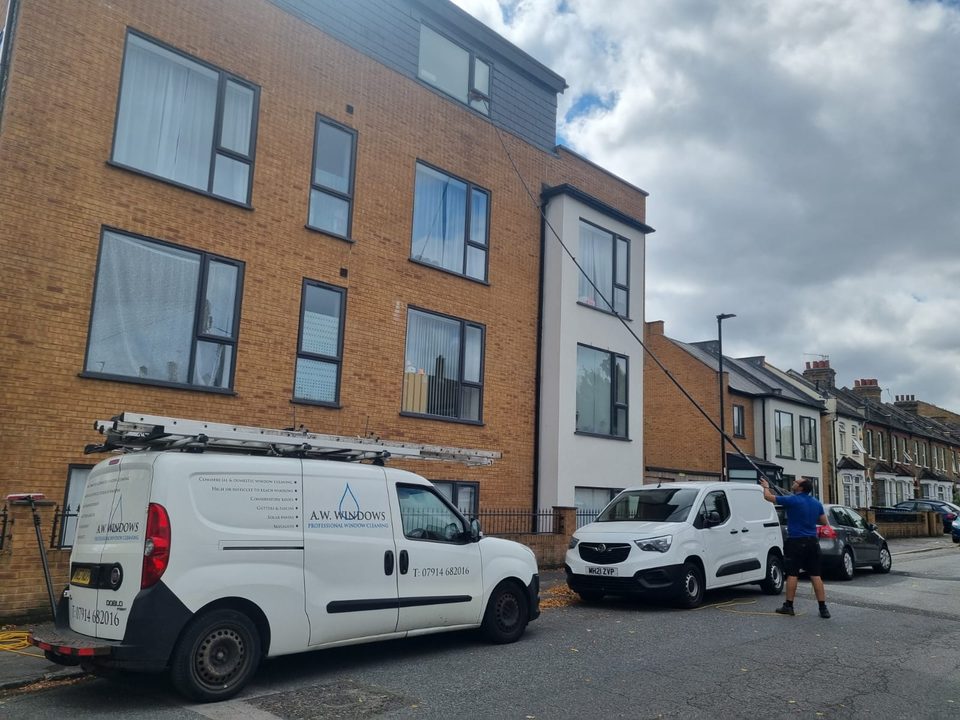 Andrew from A.W. Windows cleaning the top floor windows of a block of flats with a water-fed pole, the A.W. Windows van parked outside