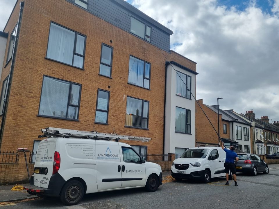 Andrew cleaning the windows of a block of flats with a water-fed pole, the A.W. Windows van in front