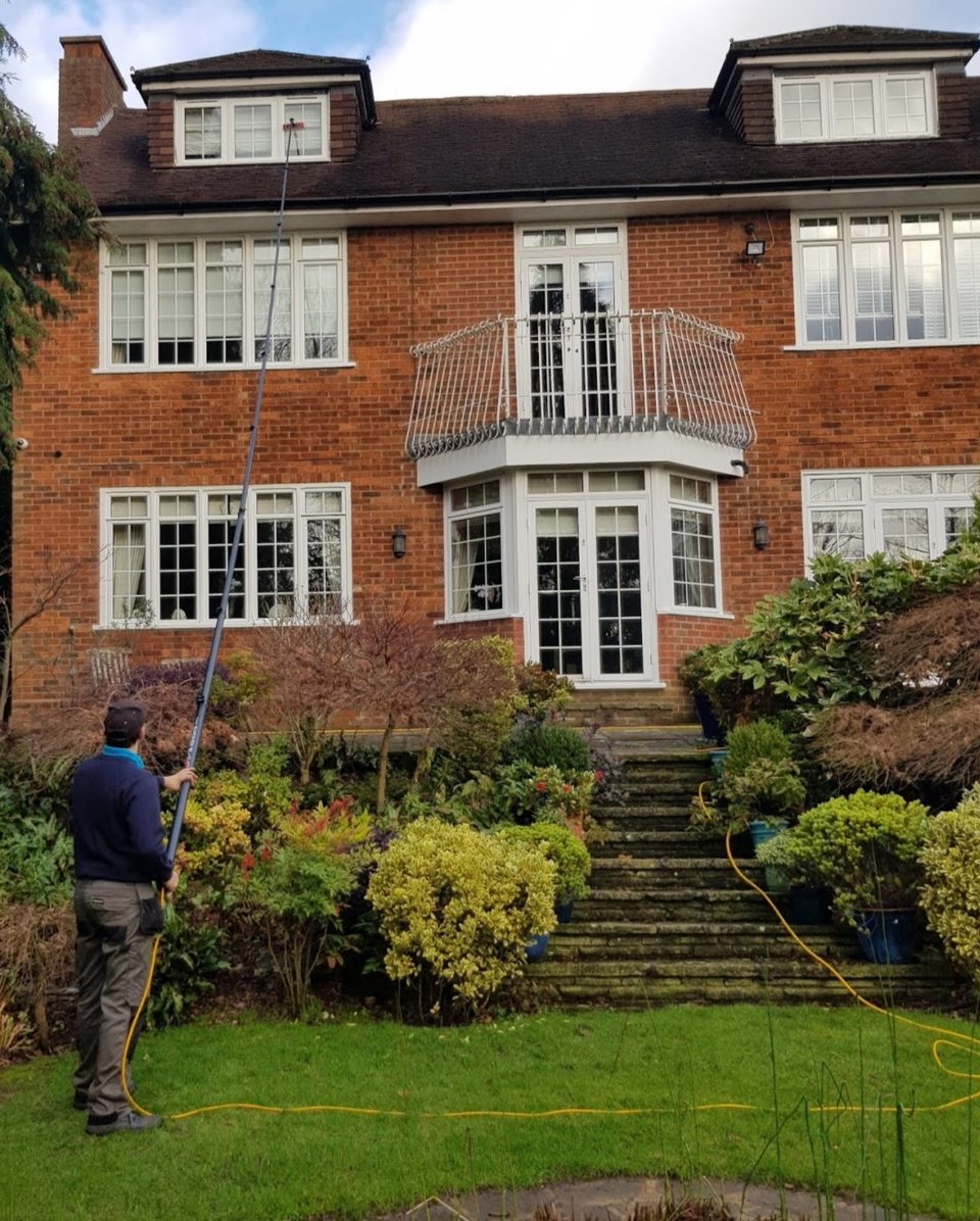 Andrew cleaning the upper windows of a large brick house from the lawn with a water-fed pole
